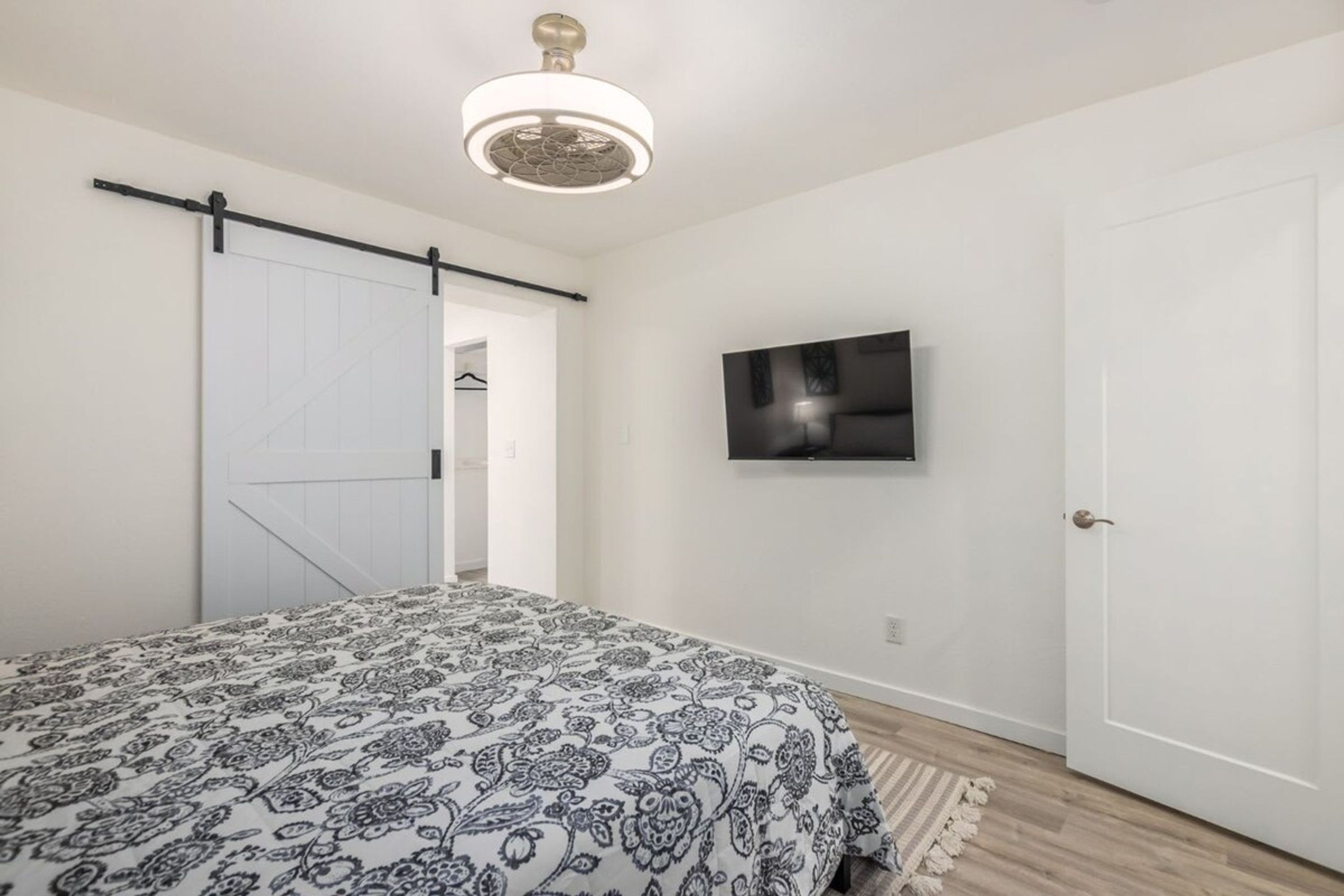 Un dormitorio con cama, puerta corrediza, televisor montado y ventilador de techo.