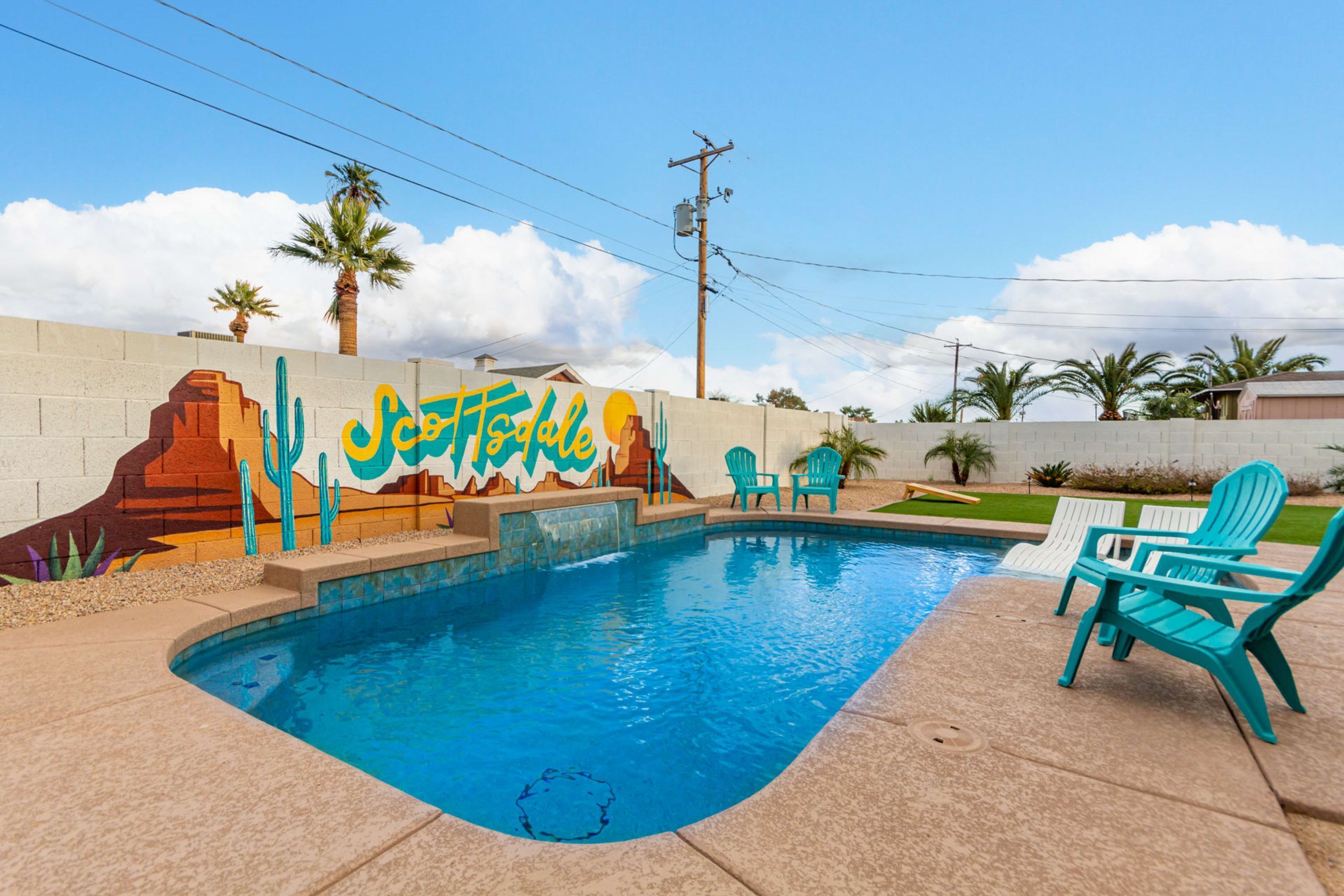 Une piscine entourée de chaises turquoise et ornée d’une fresque représentant des œuvres d’art sur le thème du désert.