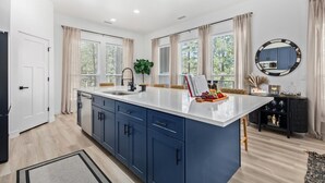 Una cocina moderna con una isla central, armarios azules y un ventanal con cortinas.