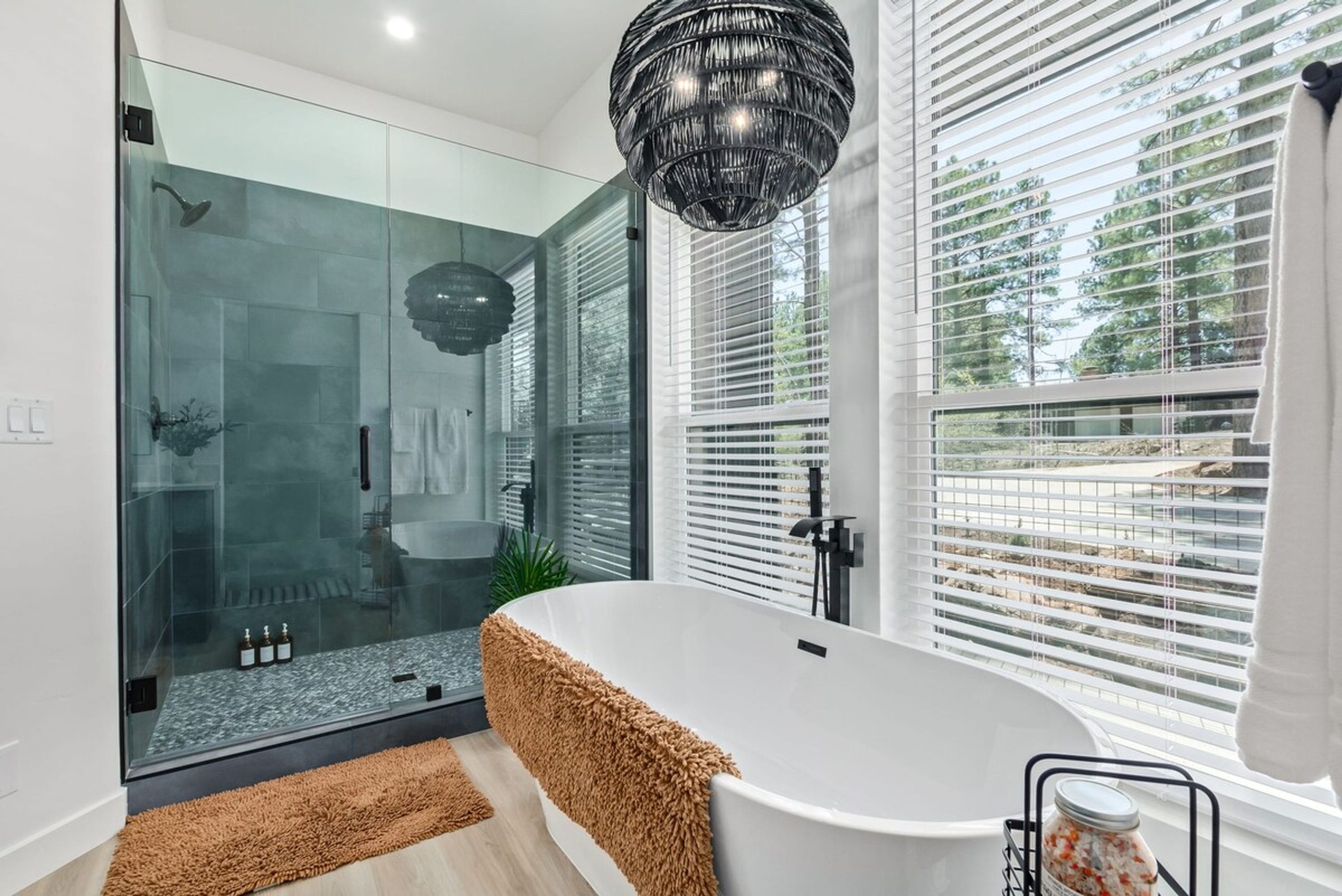 Un baño moderno con cabina de ducha de vidrio, una bañera grande y vistas al exterior a través de amplios ventanales.