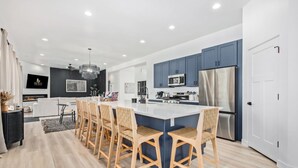 Una cocina moderna con una isla central, armarios azules, electrodomésticos de acero inoxidable y una zona de comedor con sillas de madera.