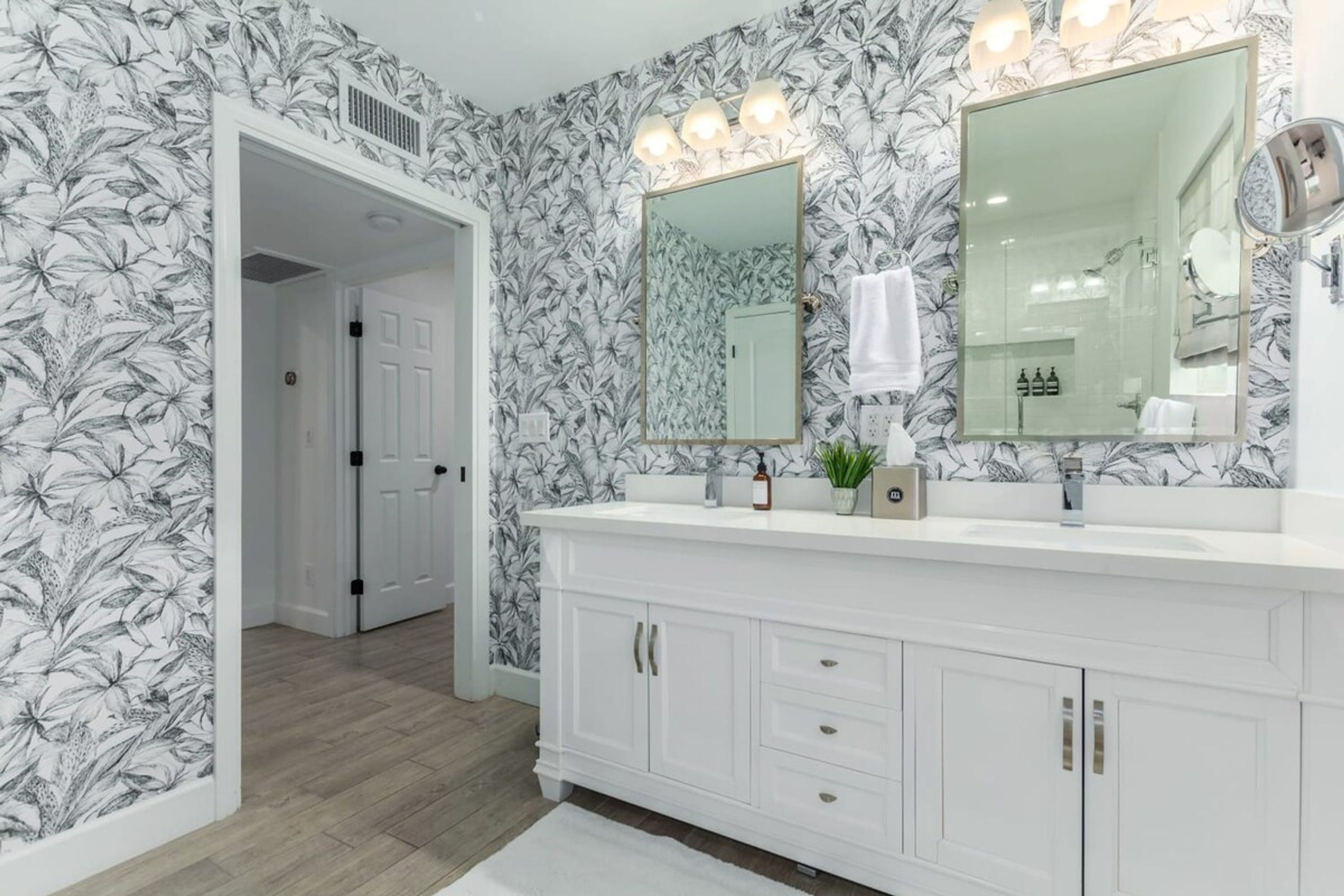A bathroom with a white vanity, two mirrors, and a floral wallpaper design.