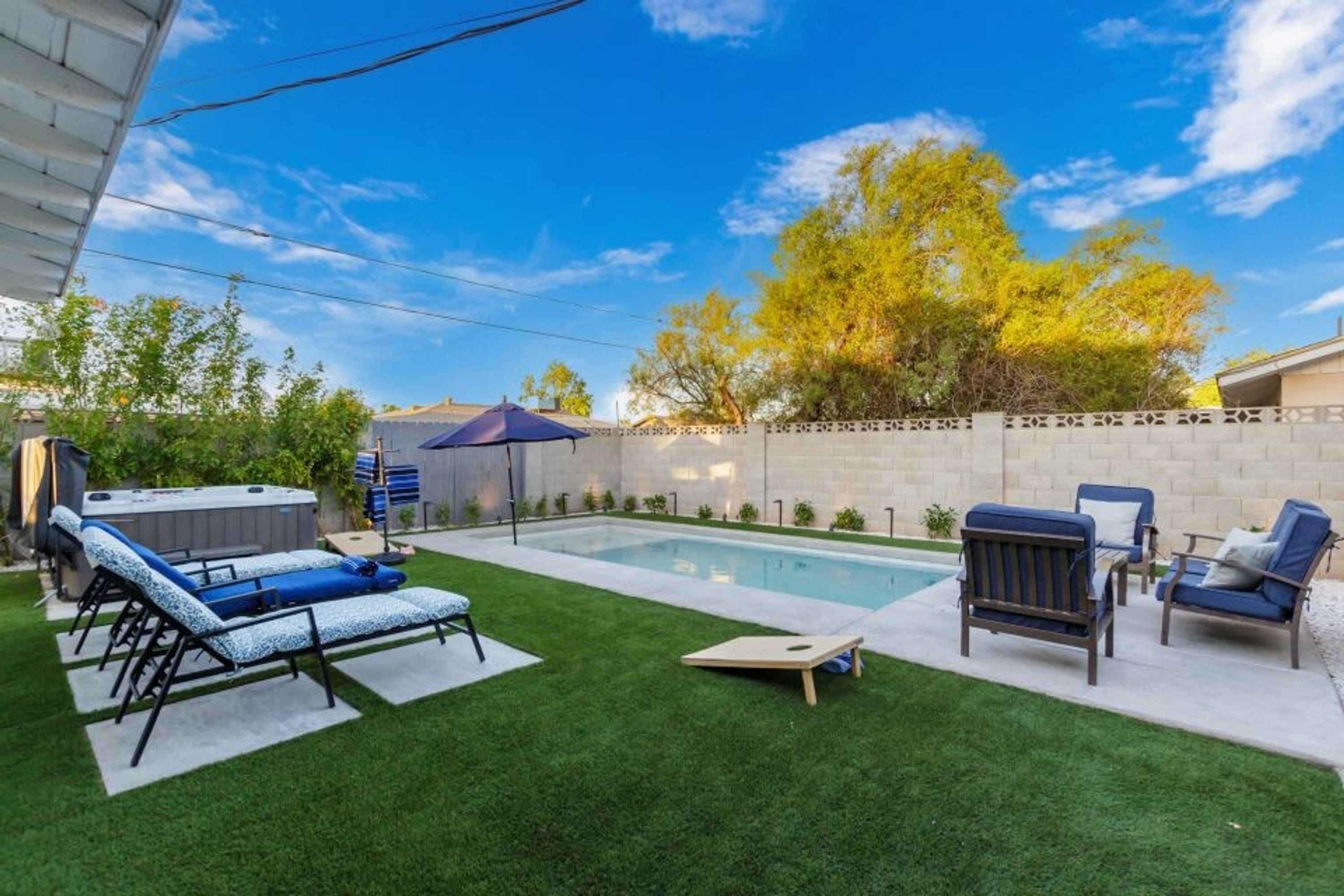 A backyard with a swimming pool, artificial grass, lounge chairs, and a hot tub.