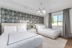 A modern hotel room with two beds, a patterned wallpaper, a large window with curtains, and a ceiling light fixture. - 8BR Villa Heated Pool Putt Grn Billiards Sleeps 18 (Phoenix)