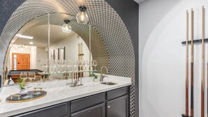 A kitchen with a marble countertop, dark cabinets, and a glass display case with wine glasses.