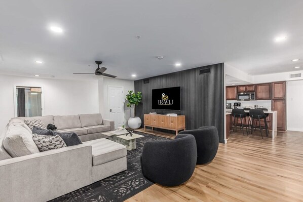 A modern living room with a grey sofa, black armchairs, and a TV mounted on the wall. - 8BR Villa Heated Pool Putt Grn Billiards Sleeps 18 (Phoenix)