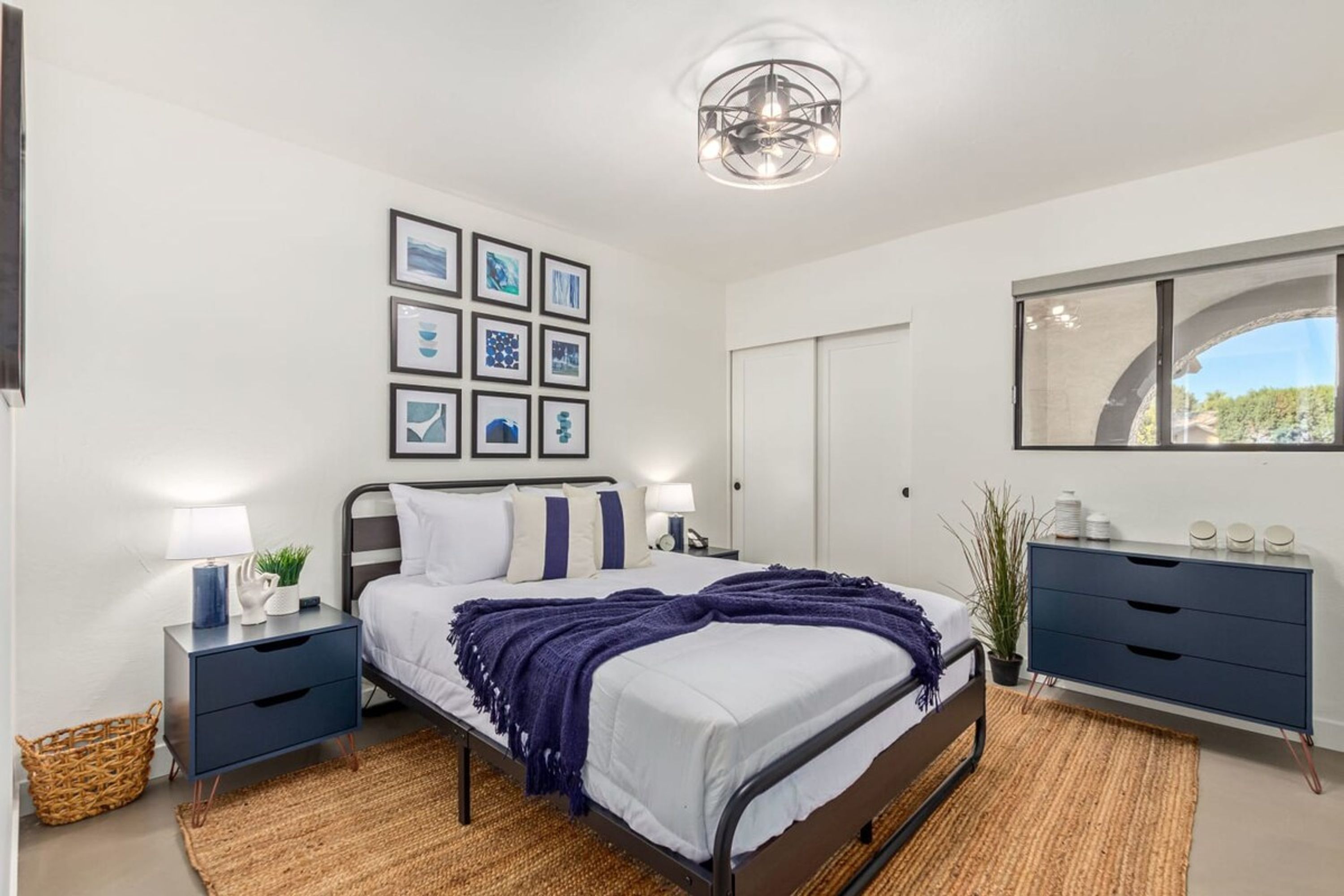 A modern bedroom with a bed, bedside tables, a dresser, and wall art.