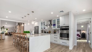 Una cocina moderna con armarios blancos, una isla de mármol y una barra central con taburetes.