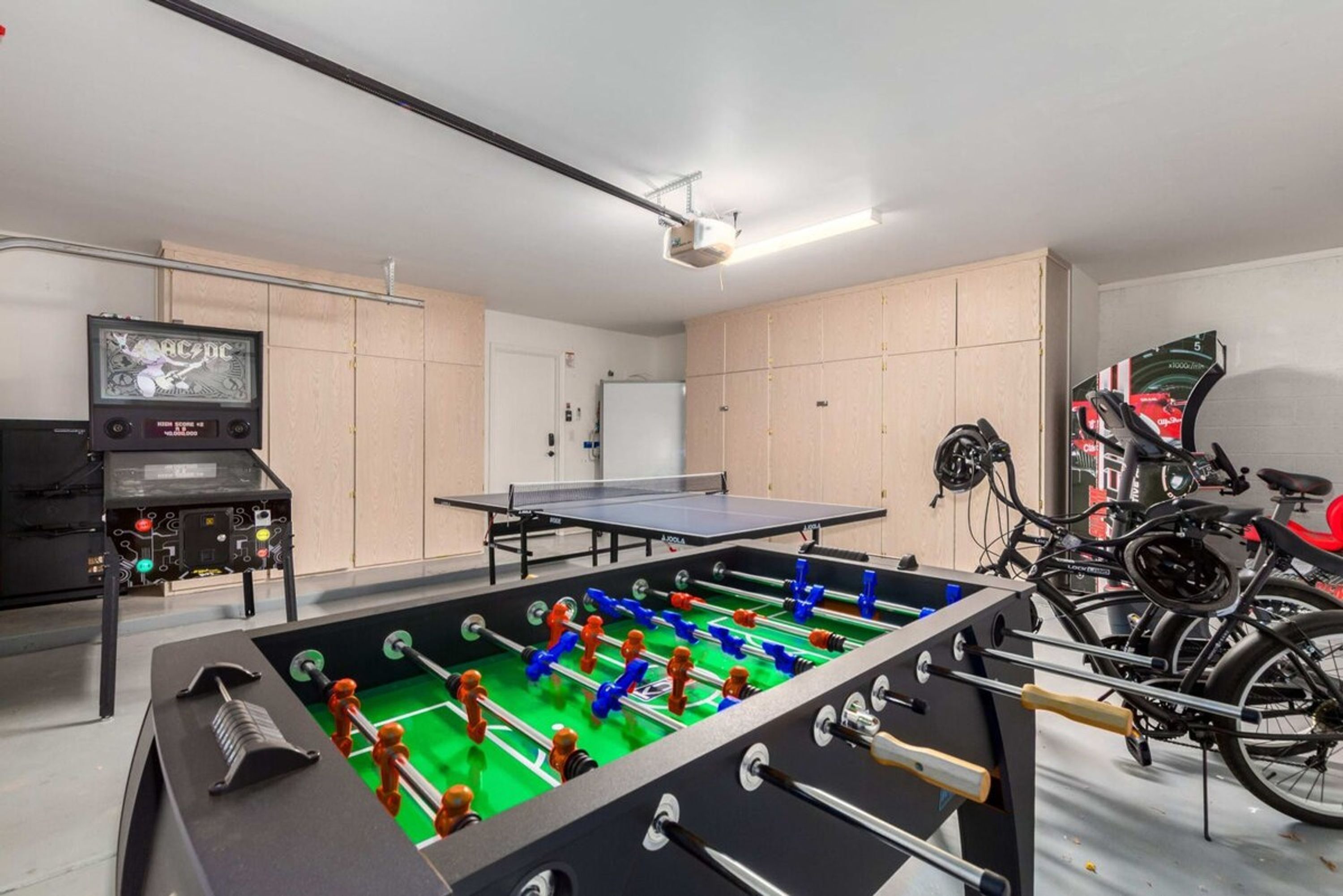 A room with a foosball table, a ping pong table, and a television displaying a music video.
