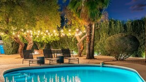 Una piscina con sillas de descanso e iluminación decorativa, rodeada de árboles y follaje.