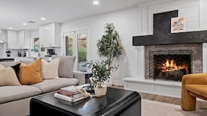Una sala moderna con chimenea, un sofá, una mesa de centro y una cocina al fondo.