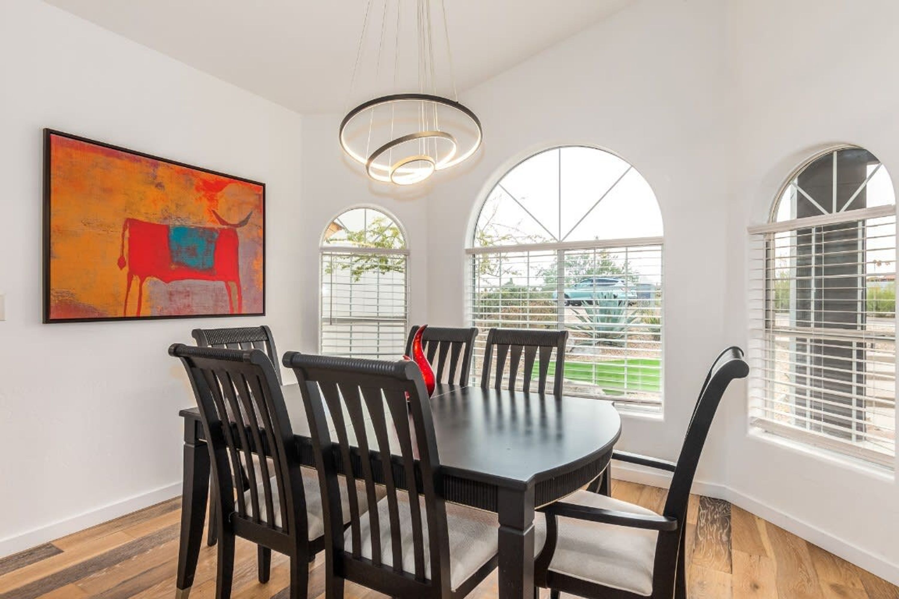 A dining area with a round table and six chairs, large arched windows, and a modern pendant light.
