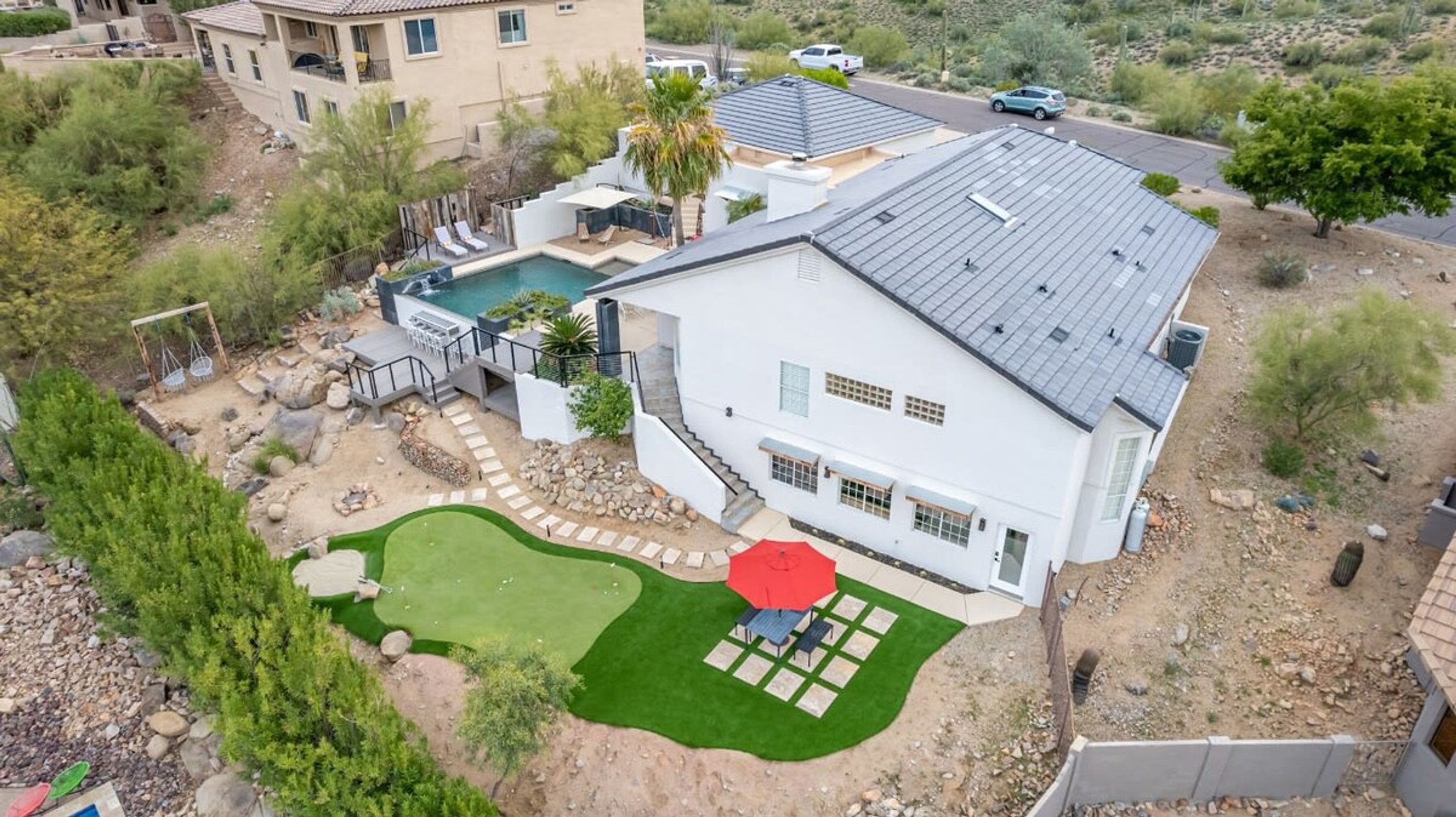 A two-story house with a swimming pool, a patio with a red umbrella, and a well-maintained lawn.