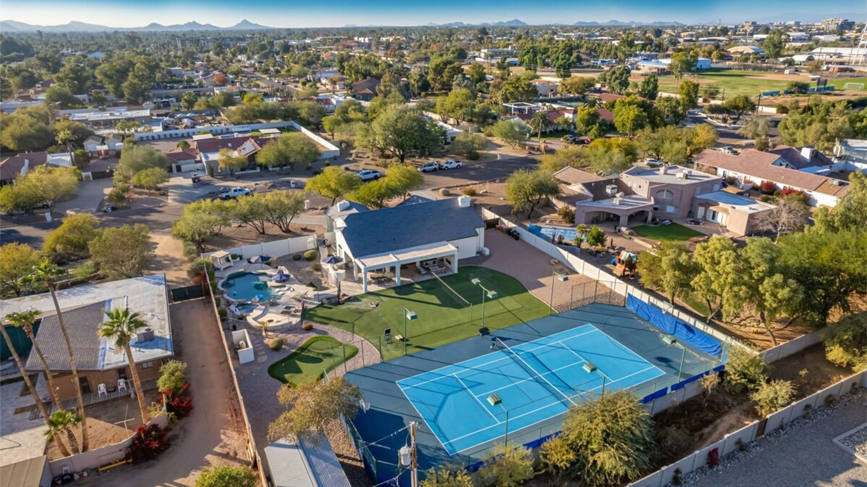 An aerial view of a residential area with houses, a tennis court, and a swimming pool.