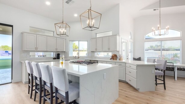 A modern kitchen with white cabinetry, a large island with bar stools, pendant lighting, and a view of the outdoors. - Sweetwater Resort Estate Tennis Pool Spa Vball (Scottsdale)