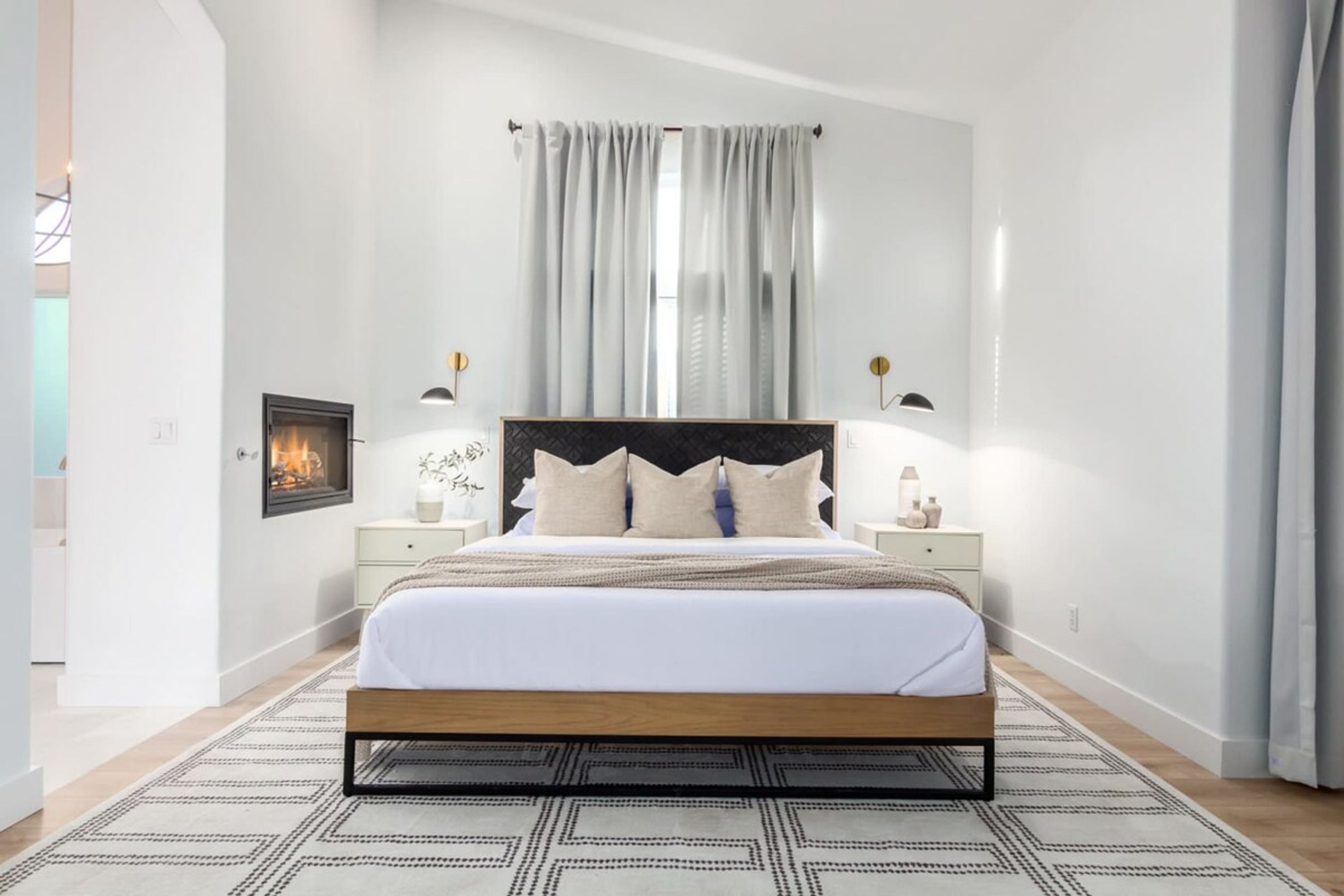 Een moderne slaapkamer met een houten bed, witte beddengoed en een vloerkleed met een geometrisch patroon.