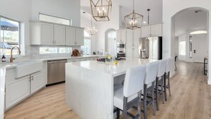 A spacious kitchen with white cabinetry, a large island with bar stools, and pendant lighting. - Sweetwater Resort Estate Tennis Pool Spa Vball (Scottsdale)