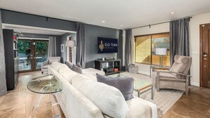 Ein modernes Wohnzimmer mit einer Couch, Sesseln, einem Glastisch und einem an der Wand befestigten Fernseher.