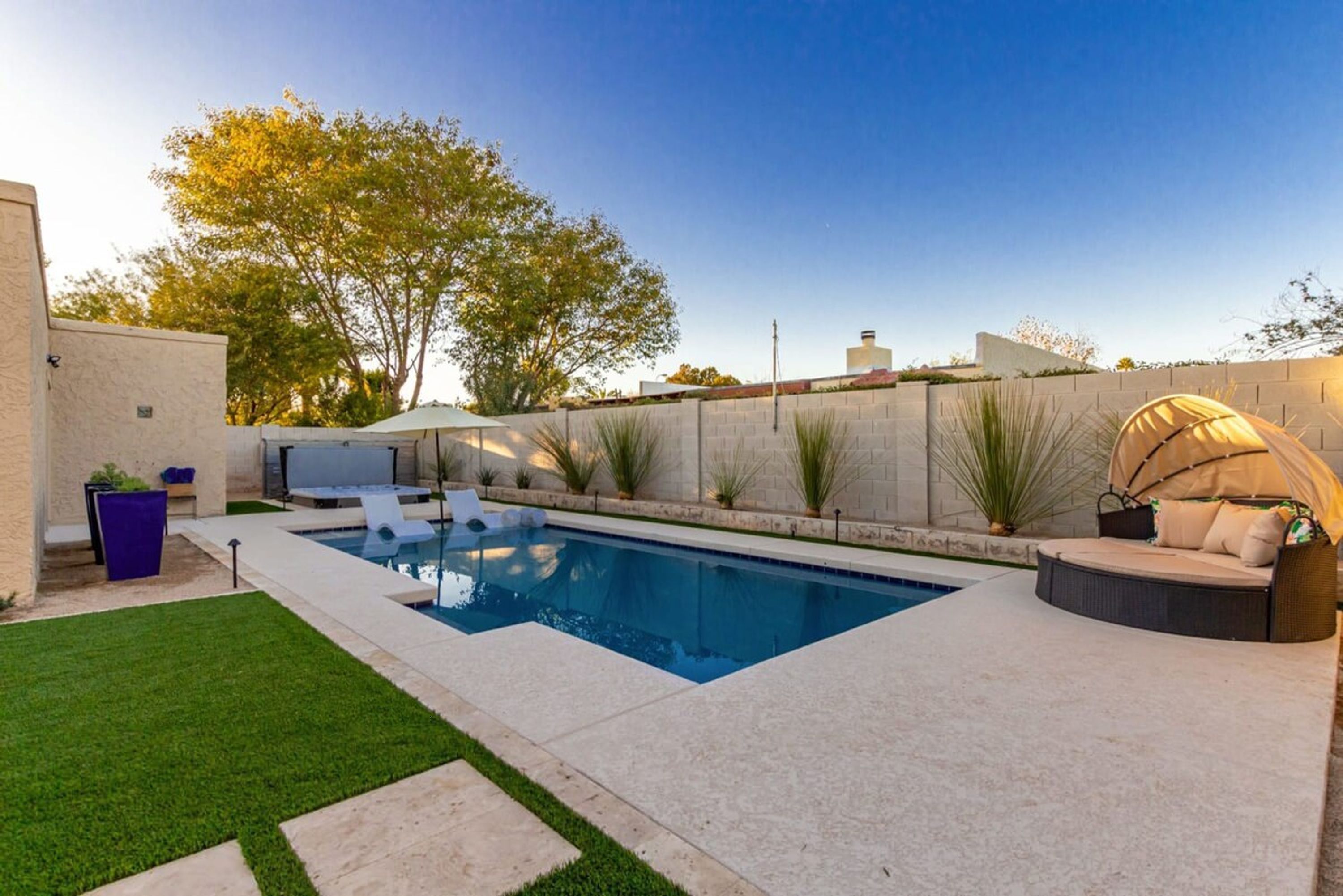 A rectangular swimming pool with a built-in seating area on one side, surrounded by a low brick wall and a grassy lawn.