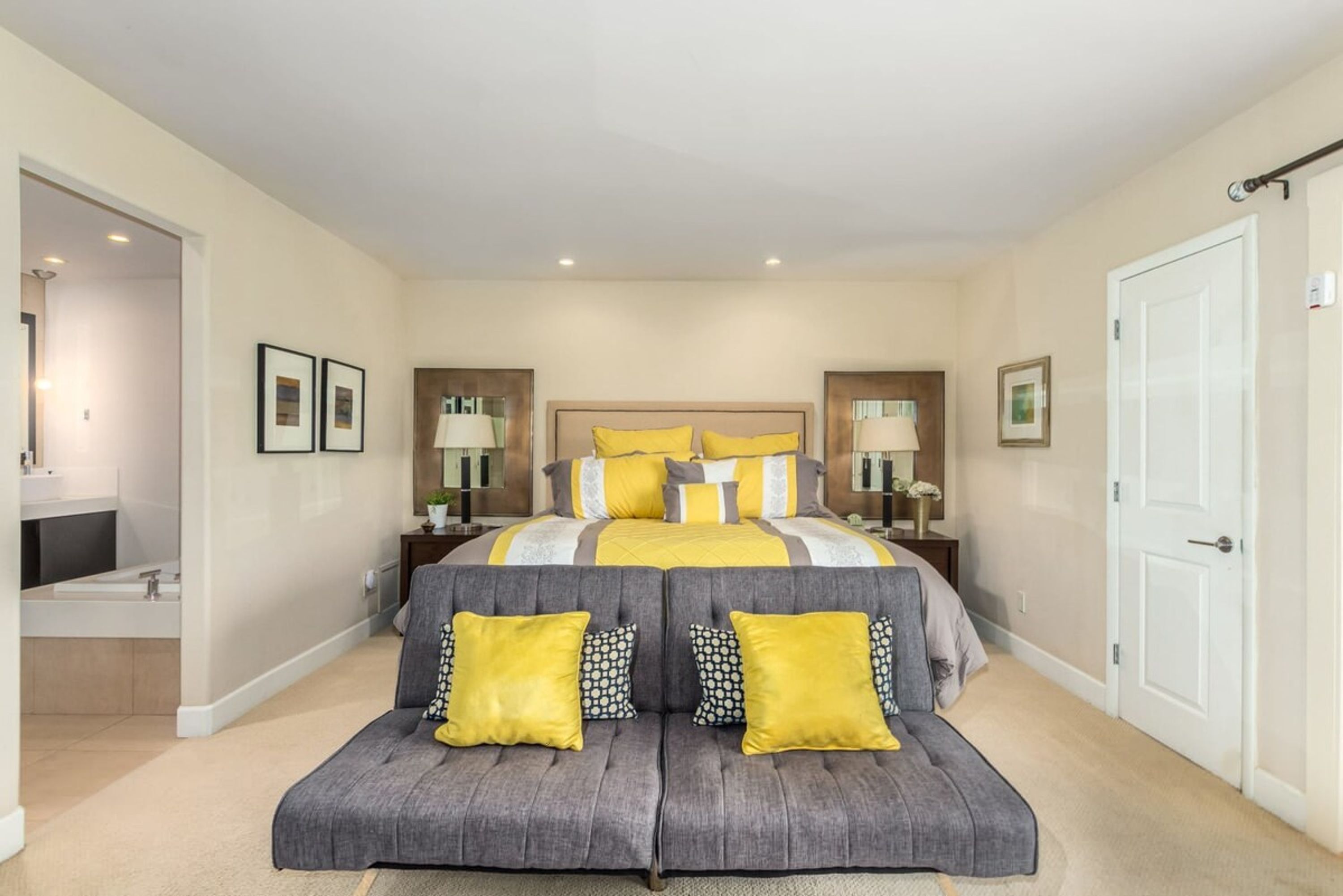 A bedroom with a large bed, bedside tables, a sofa, and a bathroom visible through an open door.