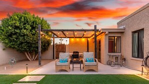 Eine Terrasse mit zwei Korbstühlen, einem Tisch und einer Pergola mit Lichterketten.