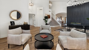 A spacious living area with a round mirror, a round coffee table, and a modern chandelier. There is a staircase leading to an upper level. - The Cardinal Walk to Stadium Pool Spa Sportcourt (Glendale)