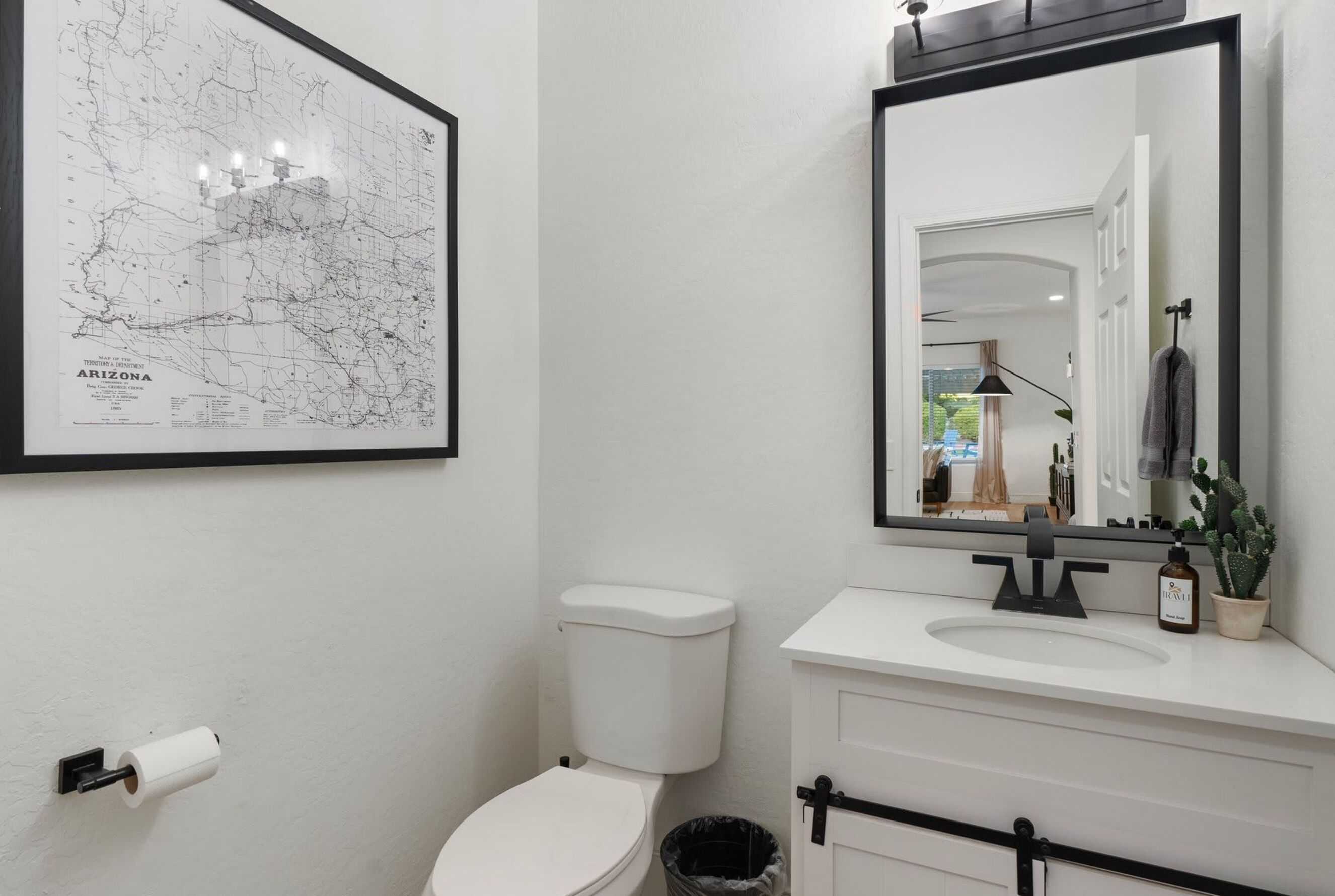 A bathroom with a white toilet, a sink, a mirror, and a framed map of Arizona on the wall.
