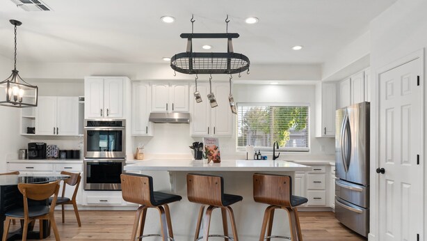 A modern kitchen with white cabinets, stainless steel appliances, and a central island with bar stools. - The Cardinal Walk to Stadium Pool Spa Sportcourt (Glendale)