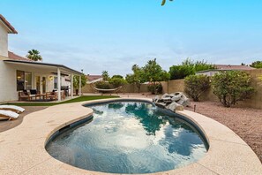 Un jardin avec une piscine, une terrasse couverte aménagée avec du mobilier d’extérieur et un mur en pierre disposé en motif de chevron.