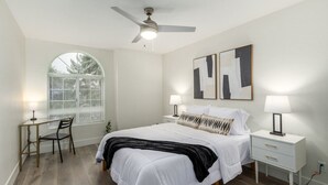 A bedroom with a bed, two bedside tables, a desk, a chair, a ceiling fan, and a window with blinds. - 5BR Citrus Estate Sleeps 13 Free Htd Pool Gameroom (Mesa)