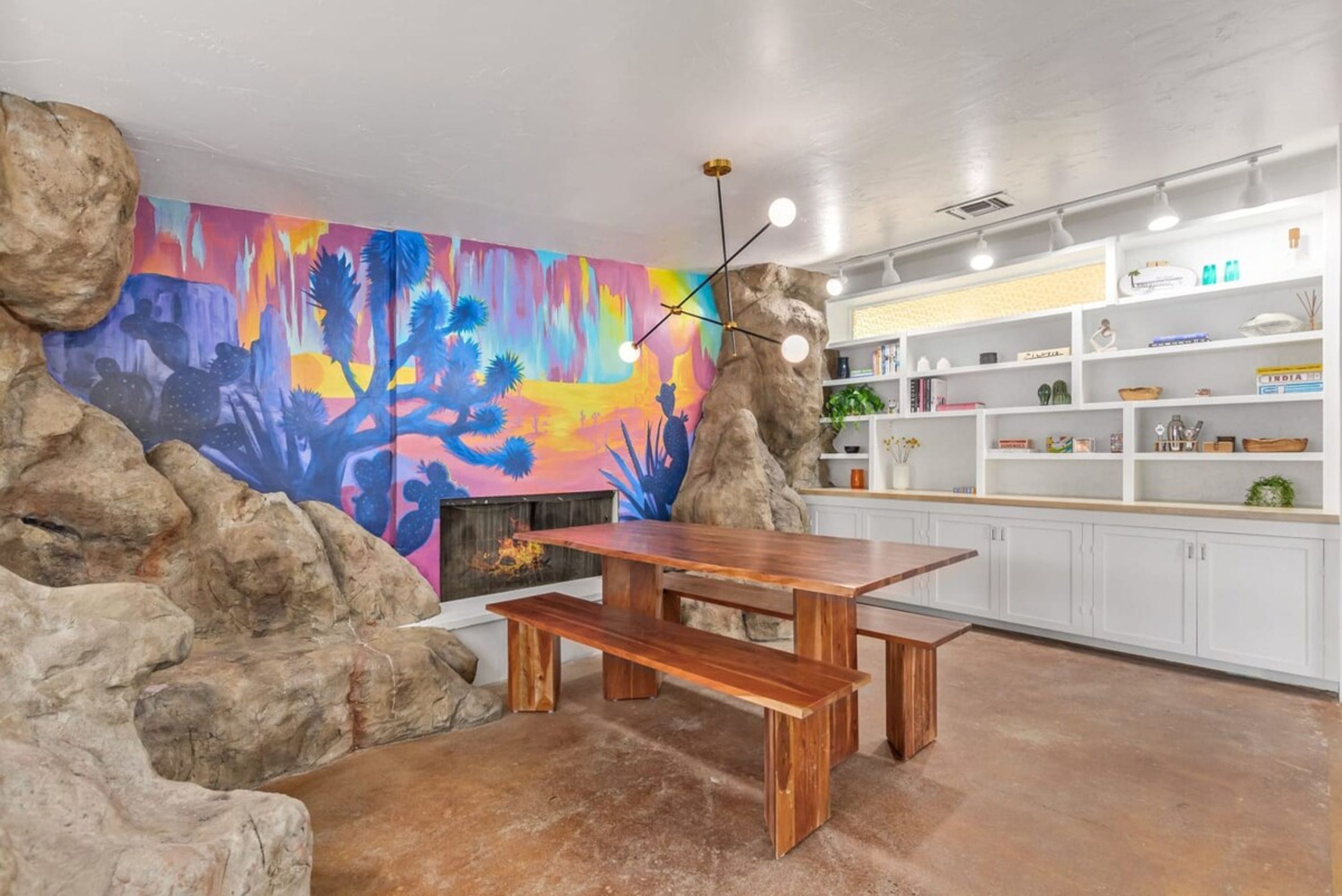Une cuisine agrémentée d’une fresque murale aux couleurs vives, d’une table en bois et de meubles de rangement blancs.