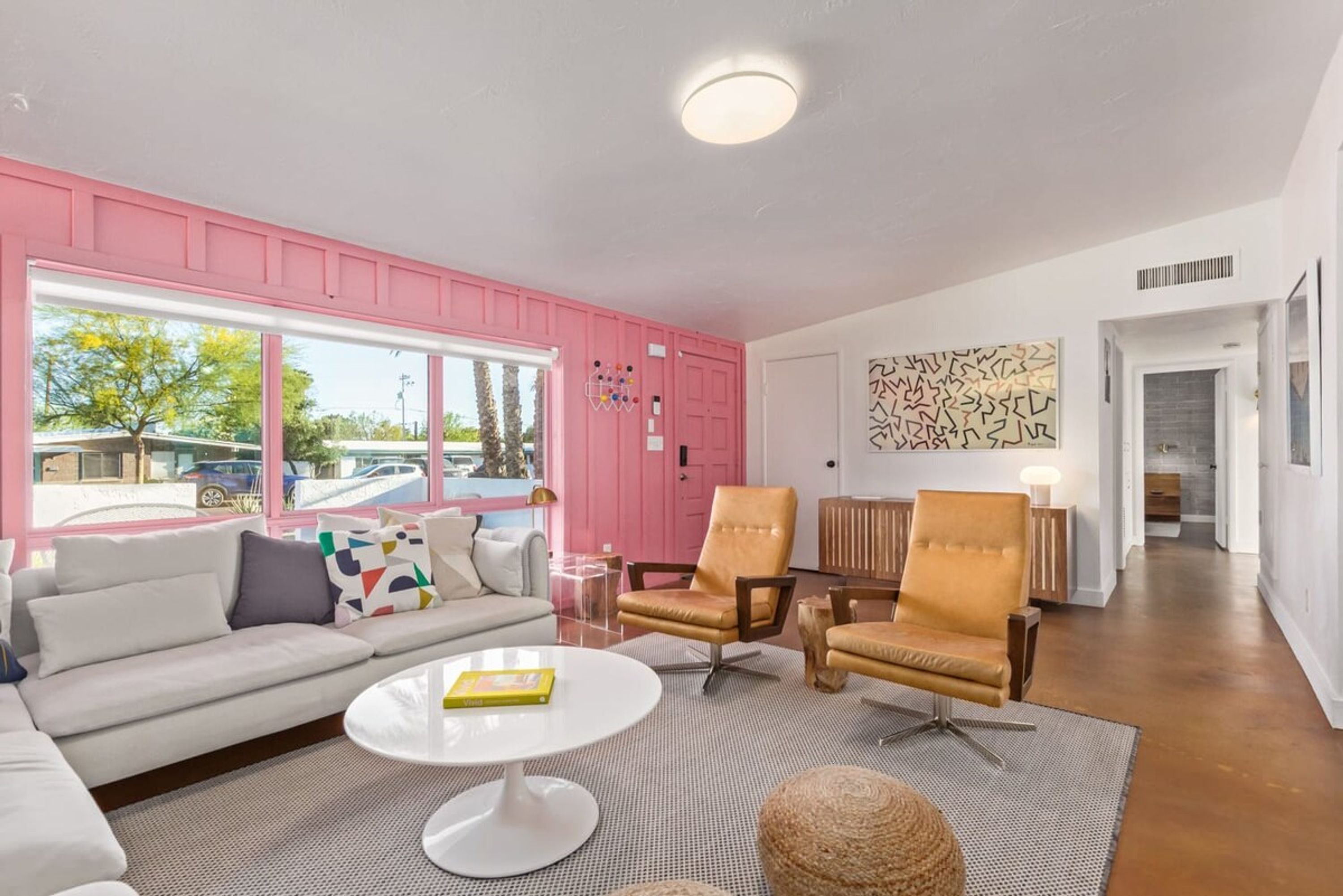 A living room with a white sofa, two armchairs, a coffee table, and a large window with pink walls.