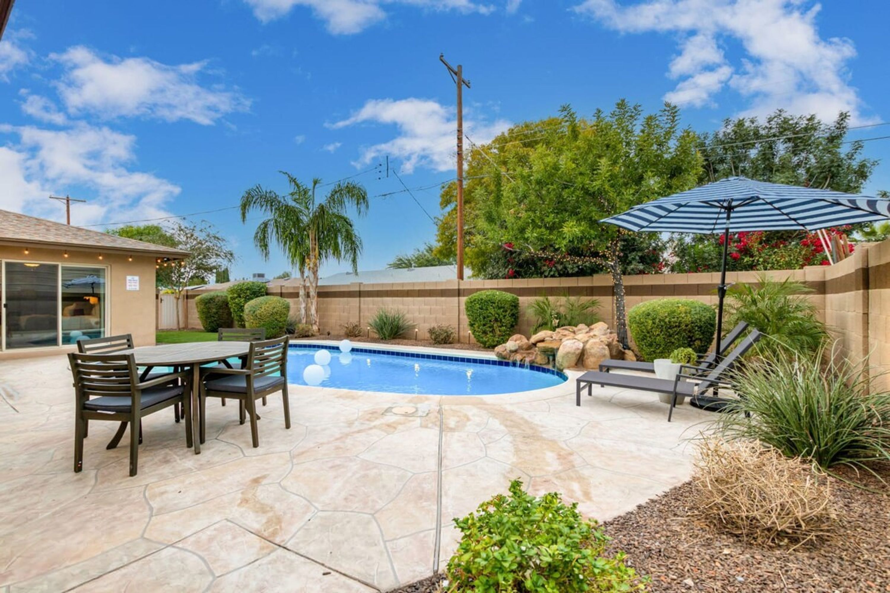 Un patio trasero con piscina, mobiliario de exterior y una zona de estar cubierta.