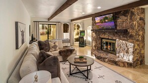 A cozy living room with a stone fireplace, a large flat-screen TV mounted above it, a sofa with plush cushions, and a coffee table with a book and a plant. - Serenity Retreat Sedona Hot Tub Games Firepit (Sedona)
