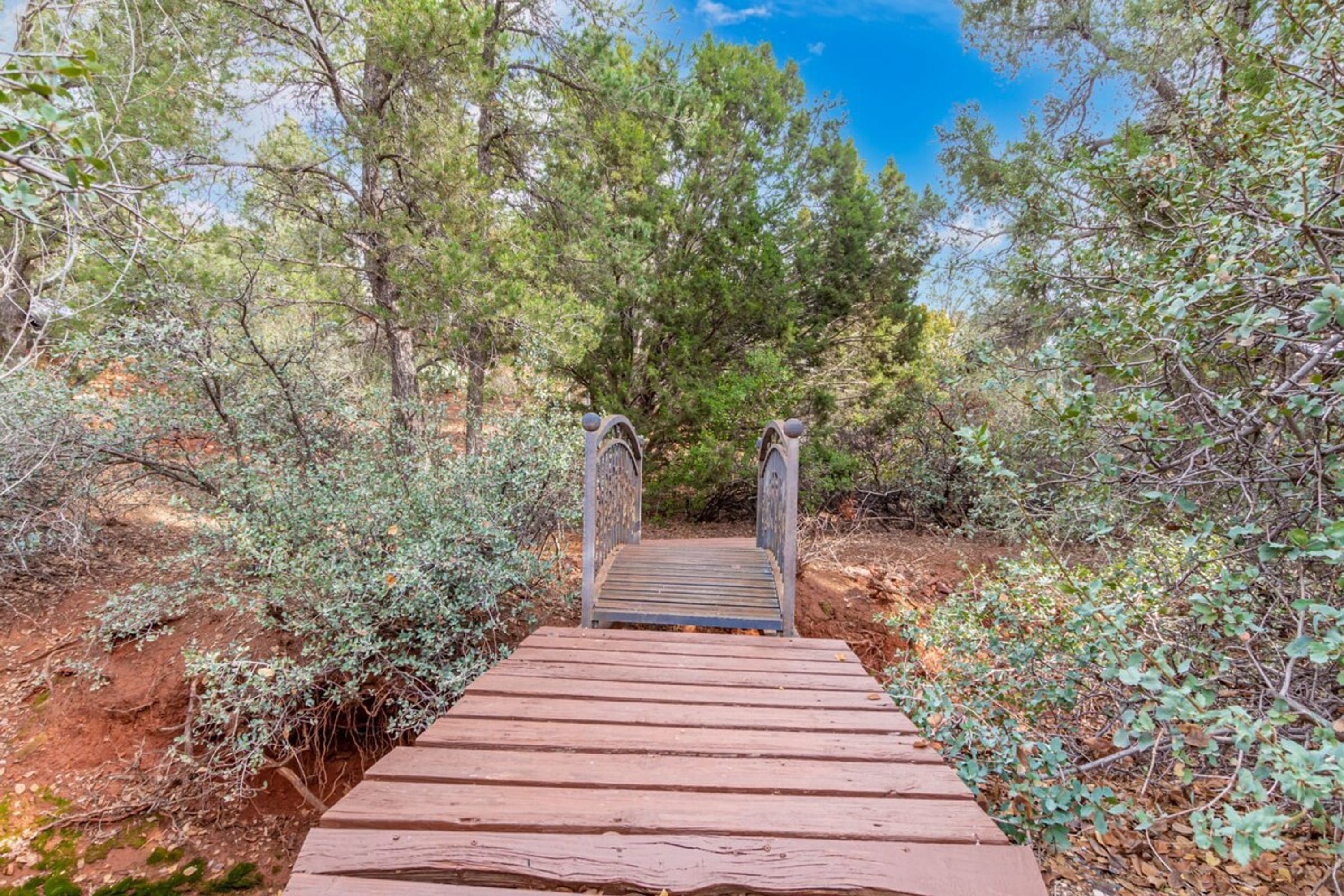 A wooden pathway leading to a gate surrounded by trees and shrubs.