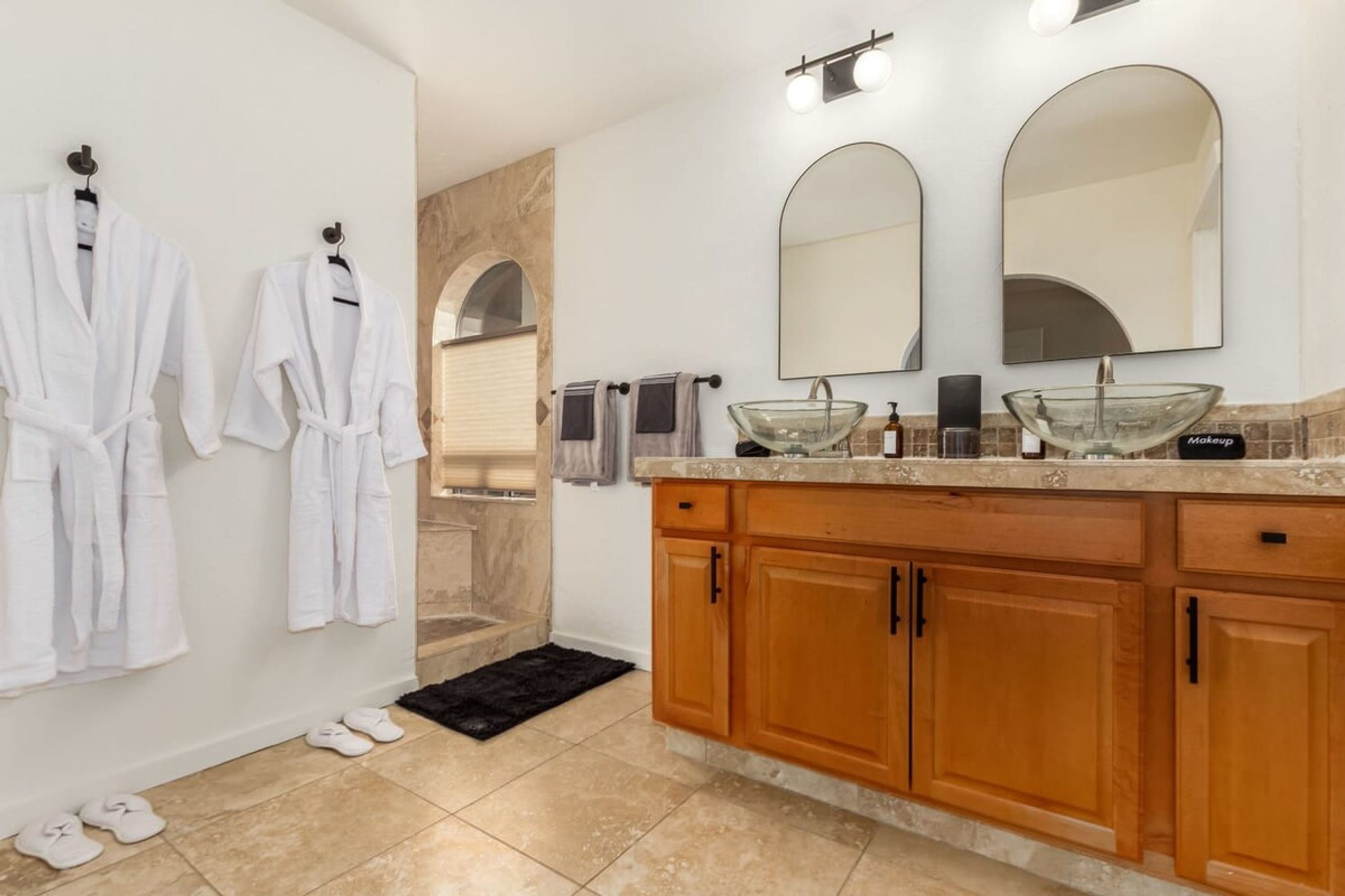 A modern bathroom with a glass sink, wooden cabinets, and two mirrors.