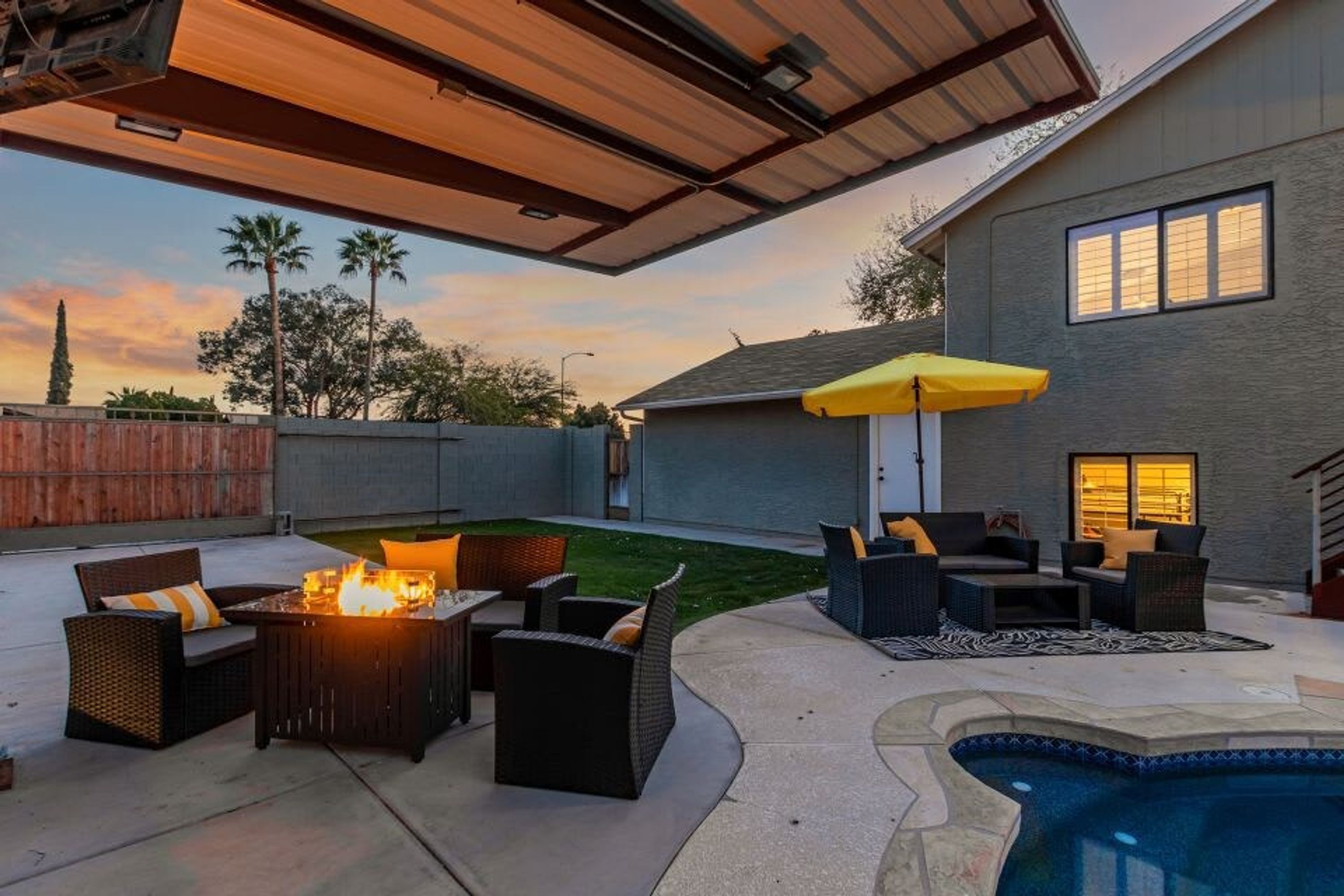 A backyard with a fire pit, outdoor furniture, a swimming pool, and a covered patio area.