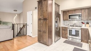 A modern kitchen with wooden cabinets, stainless steel appliances, and a grey sofa in the adjacent living area. - Princess Retreat Private Pool Firepit Sleeps 12 (Mesa)