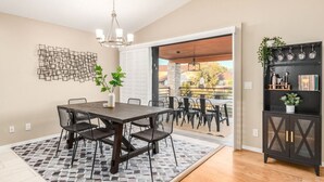 A dining area with a dark wooden table and chairs, a patterned rug, and a wall-mounted abstract art piece. - Princess Retreat Private Pool Firepit Sleeps 12 (Mesa)