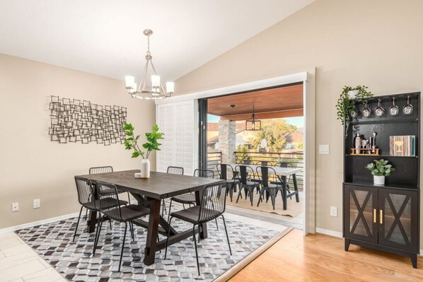 A dining area with a dark wooden table and chairs, a patterned rug, and a wall-mounted abstract art piece. - Princess Retreat Private Pool Firepit Sleeps 12 (Mesa)