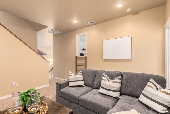 A living room with a gray sofa, striped pillows, a coffee table with decorative items, and a framed picture on the wall. - Amberwood Estate w 5 Showers Spa Mtn Views (Flagstaff)