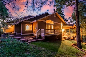 A two-story log cabin with a covered porch and a deck, surrounded by trees and a well-maintained lawn. - Amberwood Estate w 5 Showers Spa Mtn Views (Flagstaff)