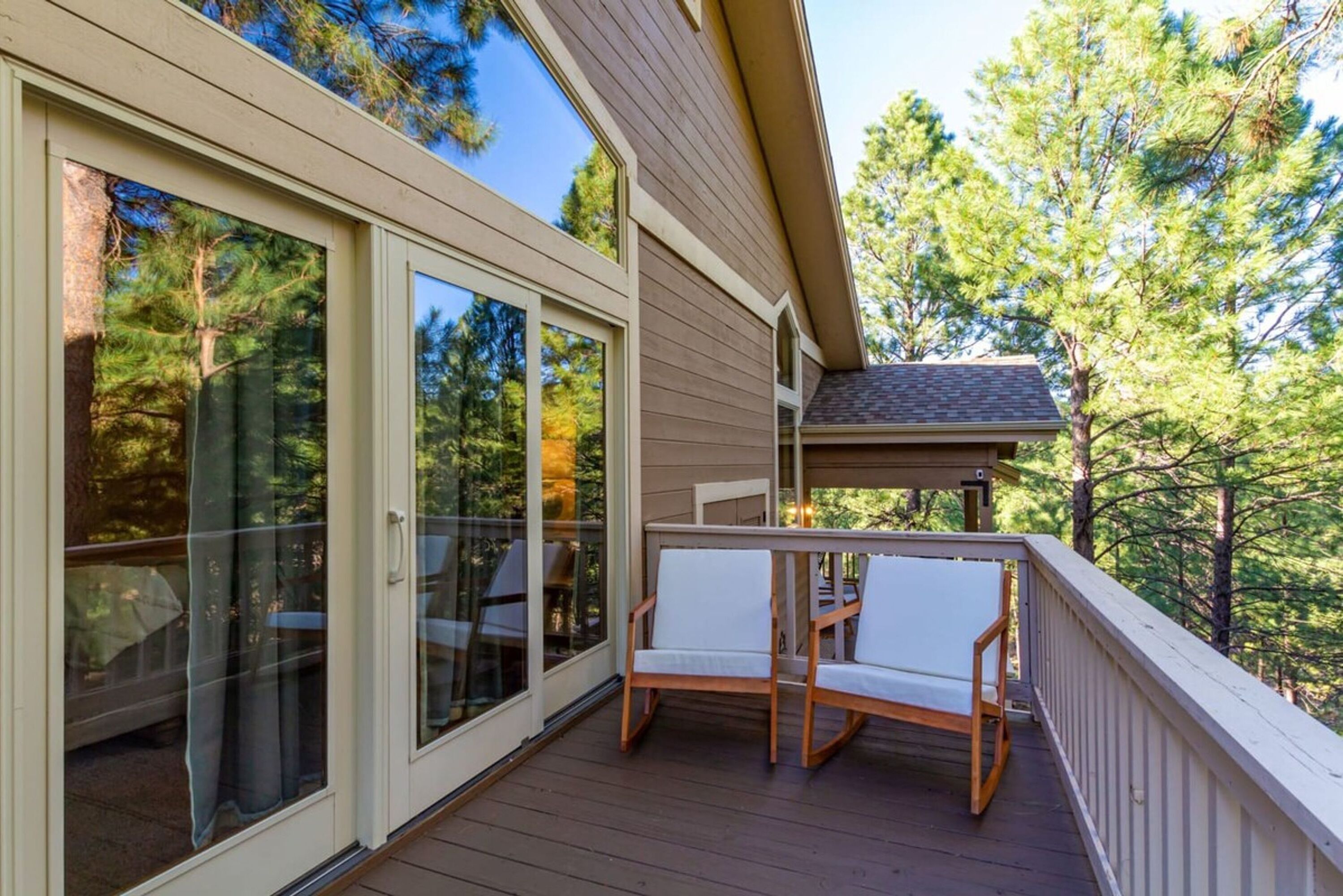 A wooden deck with two white chairs and a table, overlooking a forested area.
