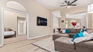 A spacious living room with a large sofa, a ceiling fan, and a wall-mounted TV displaying 'Old Town Rental'. - Walk 2 TPC Mayo Swim Putt Grill Heated Pool (Scottsdale)
