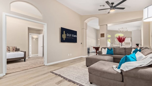 A spacious living room with a large sofa, a ceiling fan, and a wall-mounted TV displaying 'Old Town Rental'. - Walk 2 TPC Mayo Swim Putt Grill Heated Pool (Scottsdale)
