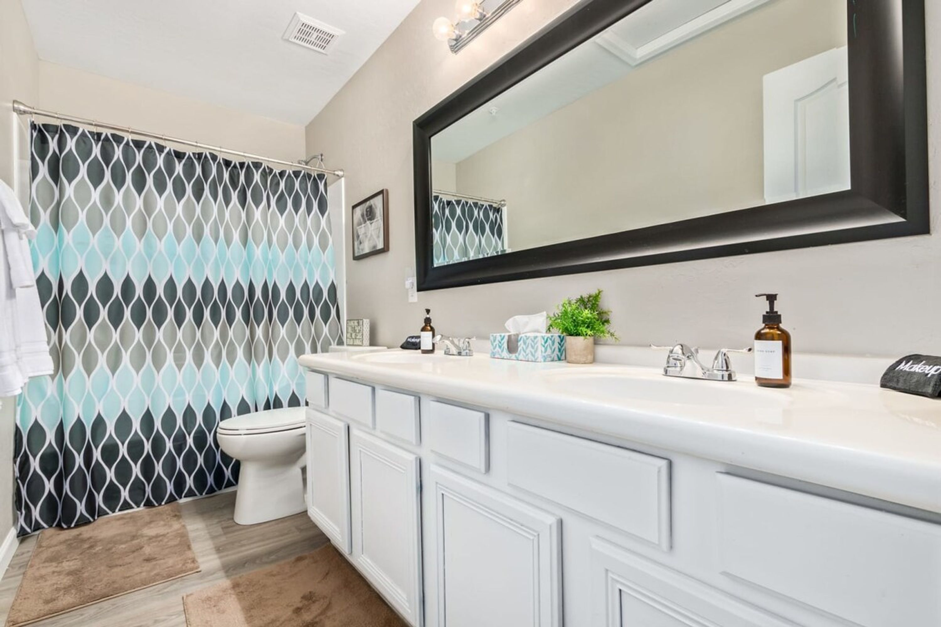 A bathroom with a white vanity, a large mirror, a shower curtain with a geometric pattern, and a toilet.
