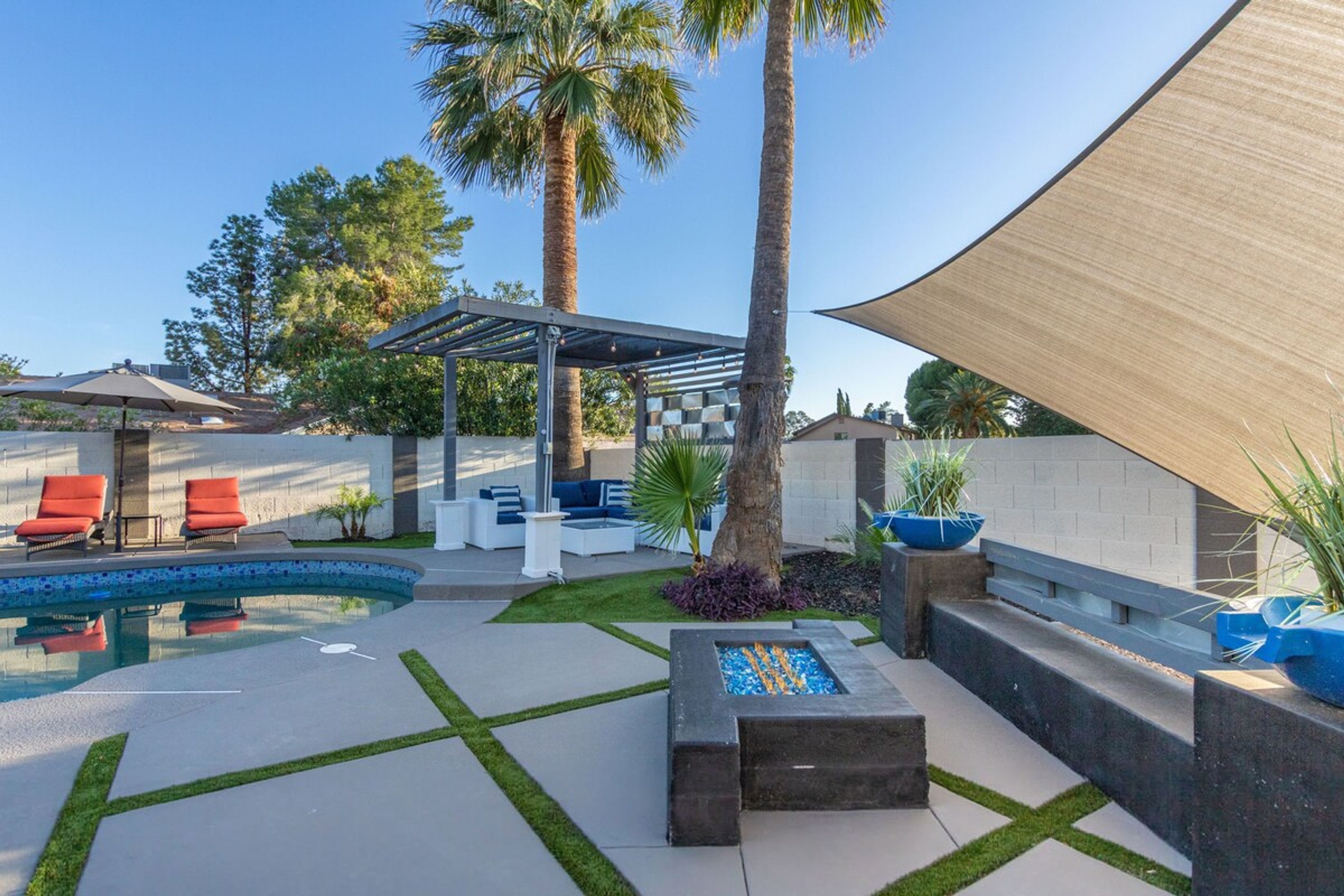 En moderne udendørs terrasse med pool, liggestole og et overdækket siddeområde.