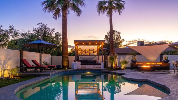 A swimming pool with lounge chairs and a fire pit area, surrounded by palm trees and a sunset sky. - Kings Lux Escape Free Htd Pool Cabana BBQ Firepit (Scottsdale)