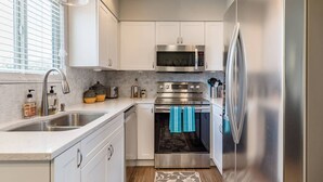 A modern kitchen with white cabinets, stainless steel appliances, a double sink, and a window with blinds. - Rustic Modern Townhouse Old Town 4 Heated Pools (Scottsdale)