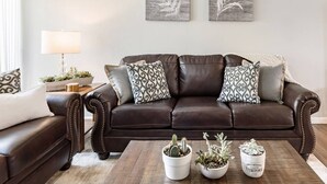 A brown leather sofa with patterned cushions, a wooden coffee table with potted plants, and a side table with a lamp and decorative items. - Rustic Modern Townhouse Old Town 4 Heated Pools (Scottsdale)